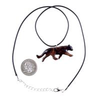 A dark reddish-brown wooden panther necklace pendant hangs from a black cord necklace. The pendant is carved in the shape of a panther in motion.  The necklace includes a silver clasp. A quarter is shown for scale.