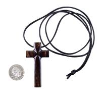 A dark brown wooden cross pendant on a black cord that ends in a knot. The pendant sits next to a quarter to show scale. It has a glossy smooth finish showing the wood grain.