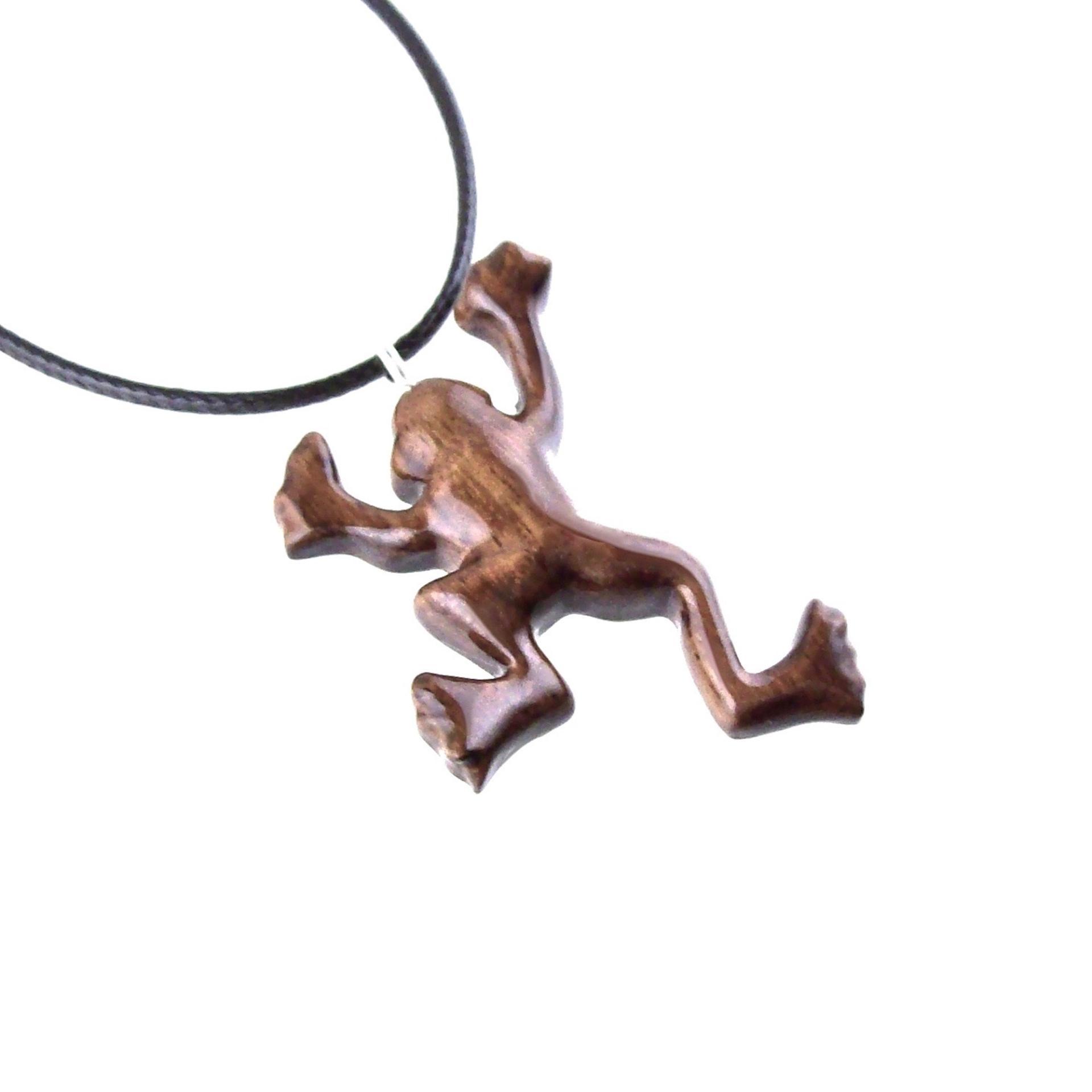 A brown frog pendant on a black cord necklace. The frog is in a jumping pose with its legs outstretched.