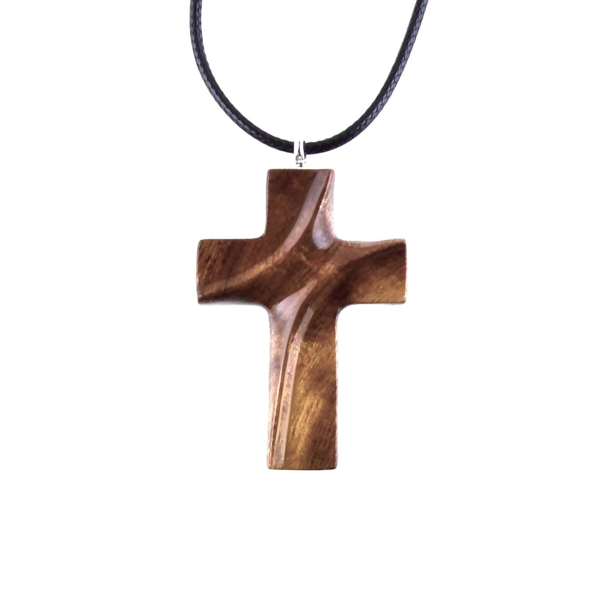 A wooden cross pendant necklace carved in brown wood with black cord. The pendant is intricately detailed and shows the wood grain. This handcrafted necklace is a unique and stylish accessory.