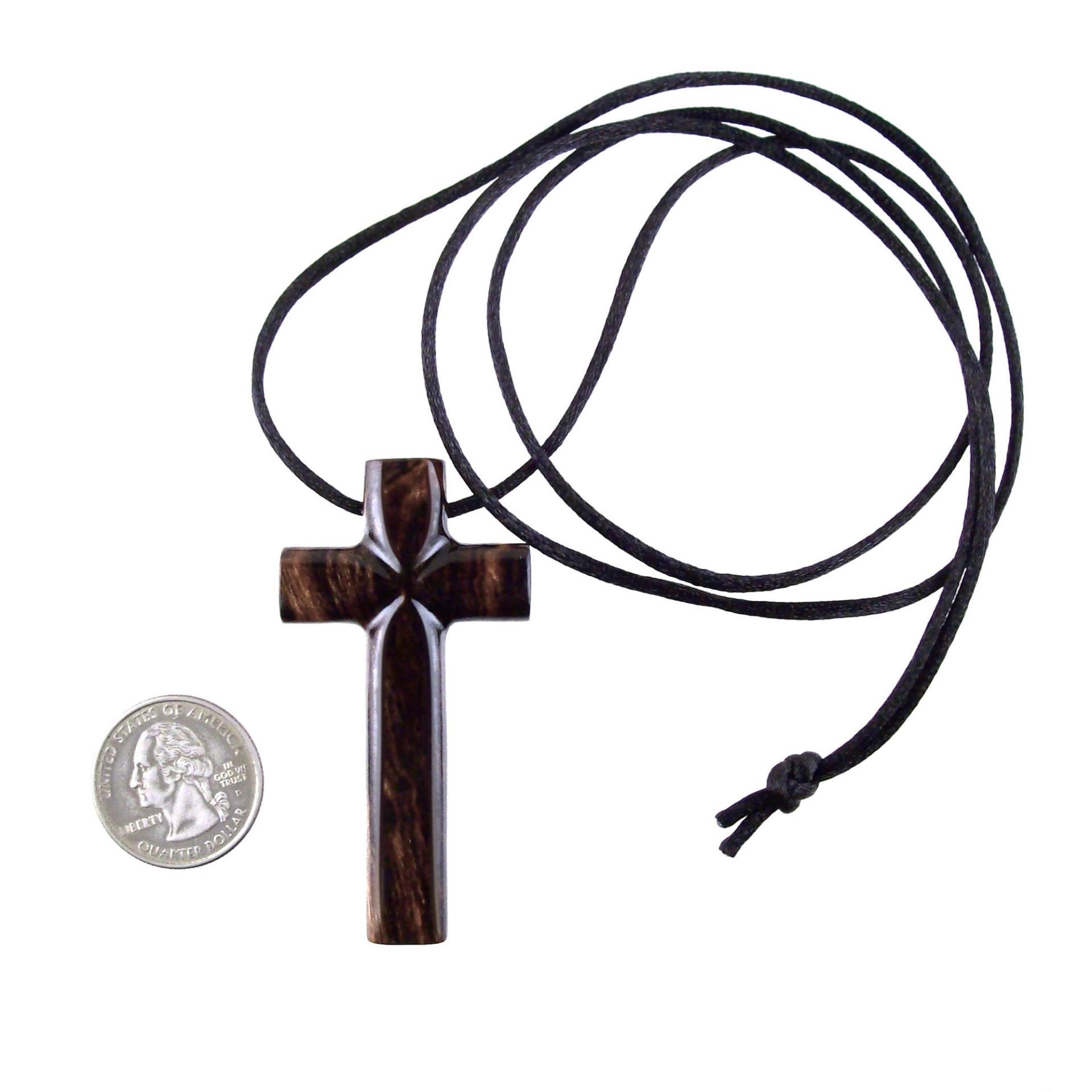 A dark brown wooden cross pendant on a black cord that ends in a knot. The pendant sits next to a quarter to show scale. It has a glossy smooth finish showing the wood grain.